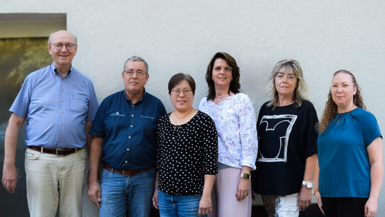 Das Team von MG Optik in Dieburg – sechs Mitarbeiterinnen und Mitarbeiter vor grauer Wand, freundlich lächelnd.